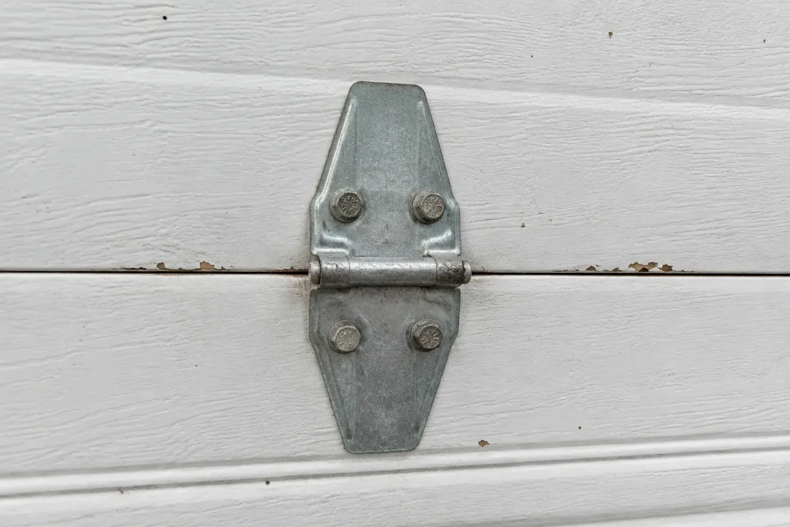 Metal center hinge across a seam in a white sectional garage door. — Garage Door Hinge Replacement, Hamilton